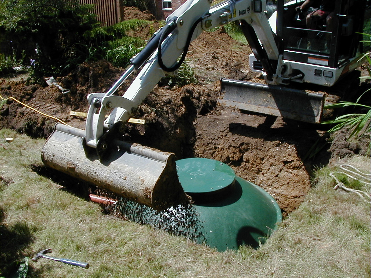 A digger covering dirt over a diamond sewage treatment plant during installation